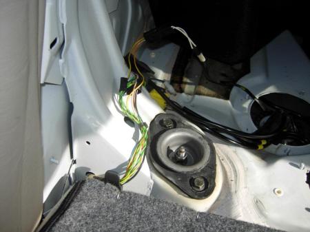 Right side shock mount on sedan located behind rear seat near fuel pump.